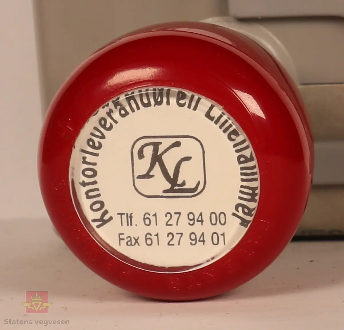 Rødt, grått, hvitt og svart stempel i plast. Firkantet med rundt håndtak. Stempel puten er tørket og har vegvesenets logo med tekst. 