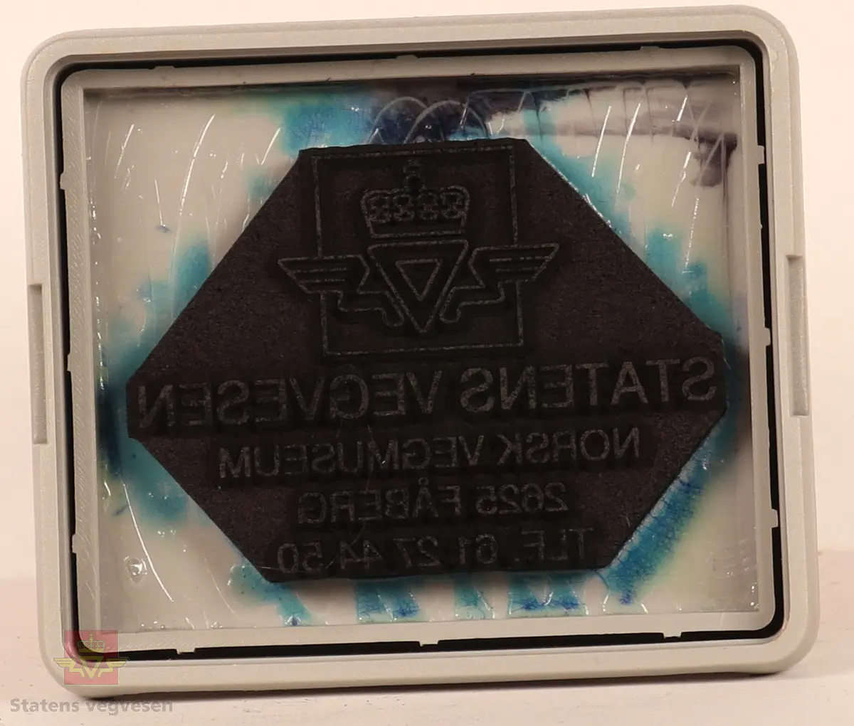 Rødt, grått, hvitt og svart stempel i plast. Firkantet med rundt håndtak. Stempel puten er tørket og har vegvesenets logo med tekst. 