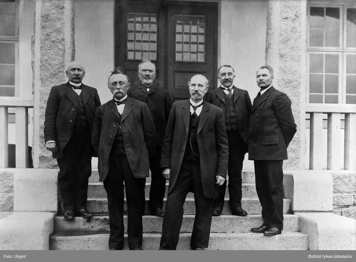 Rakkestad sparebank direksjon på trappa foran banken, 1914. 
Foran fra venstre: H. J. Heier, Ludvig Gjulem. Bak fra venstre: Kristian Edvard Jahren (1865-1937), H. Haaby, Aug.  Gjølstad, J. M. Schie (bankens kasserer i 47 år).