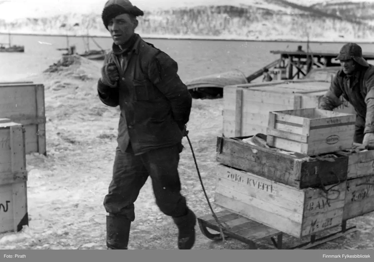 To fiskere drar slede med nyfanget fisk i trekasser fra kaien til fiskemottak i Kirkenes i mars 1941.