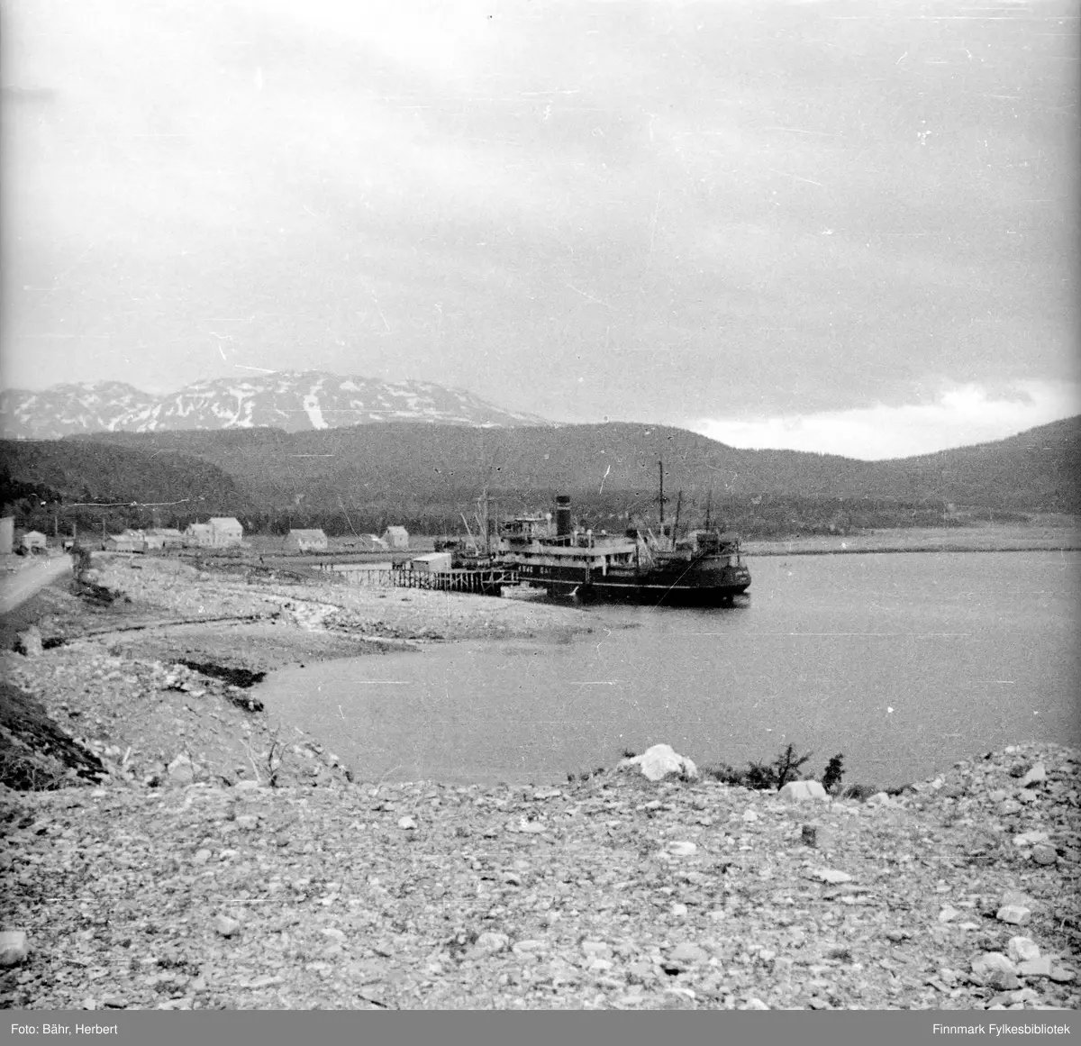 Søndenfjeldskes d/s "Kong Dag" (1862 BRT) ved kaia i Gárgu, Burfjord Kvænangen, 1942.
Gården Gárgu/ Nordkjos i bakgrunnen. I Gárgu var det posthus og telegrafstasjon.

