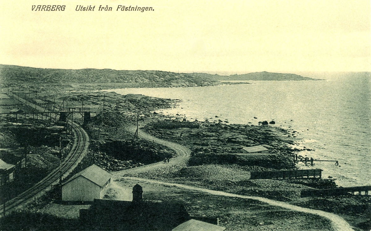 Vykort, "Varberg - Ustikt från Fästningen." Vy söderut över kustlinjen och järnvägen (Mellersta Hallands järnväg invigdes 1886). En bro leder över rälsen till Strandpromenaden och stenbrotten. Denna del av järnvägens sträckning togs ur bruk 1920. (Se även bildnr F2811.)