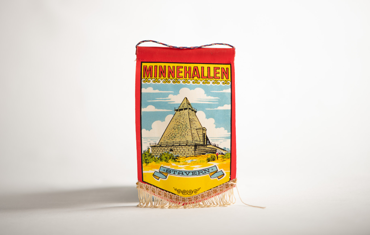 Liten vimpel/fane med "Minnehallen" i Stavern som motiv. Øverst er det en liten snor for å henge den opp med. Nederst er det påsydd gulltråd.
