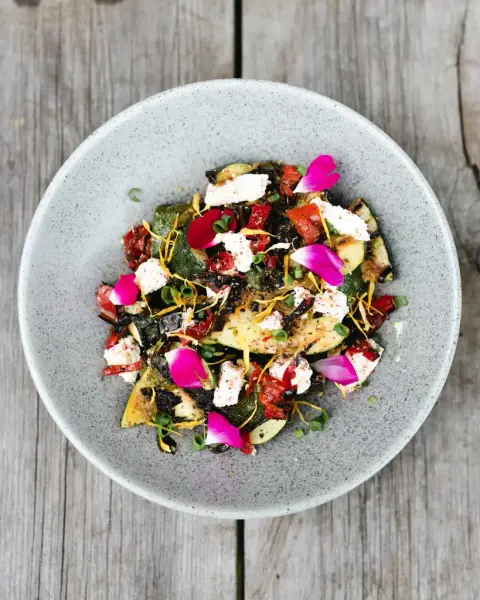 Fargerik tallerken med grønnsaker, urter, spiselige blomster og topping, servert på Gartneriet spiseri med økologiske råvarer fra kjøkkenhagen.