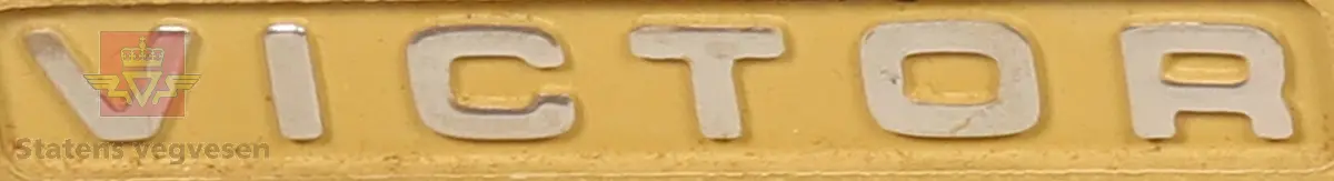 Regnemaskinen er gul med røde, oransje, brune og hvite knapper. Den har en papirrull bakerst på toppen. Tastatur panelet er grått. Har en ledning som er brun. Det hører med et gjennomsiktig deksel.
