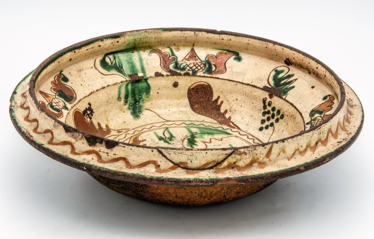 Fat av lergods, insidan täckt med vitlera med ristad dekor och grön glasyr. Märkt 1779.