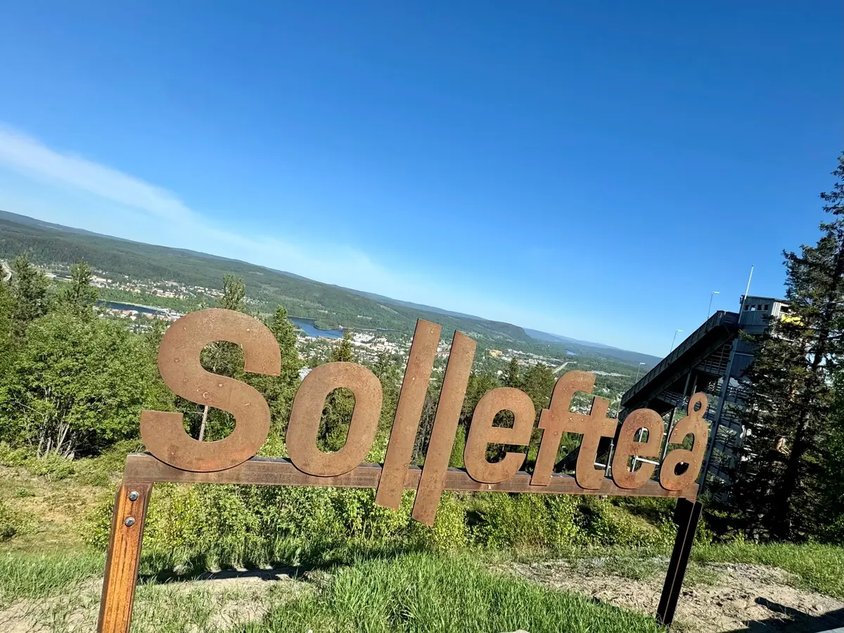 En rostfärgad skylt där det står Sollefteå mot grönska och himmel.