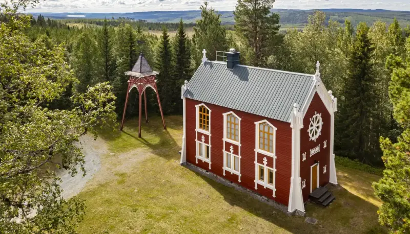 Ett rött hus och en klockstapel som står i en skog. 