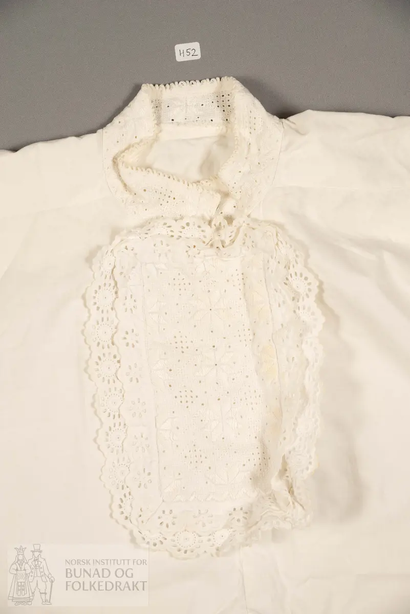 Skjorte, nattskjorte. Sauma av kvit bomullslerret. Glatt isydde ermar. Skulderstykke, og formklipt halsopning. Brodert smekke, halskrage og ermelinningar.