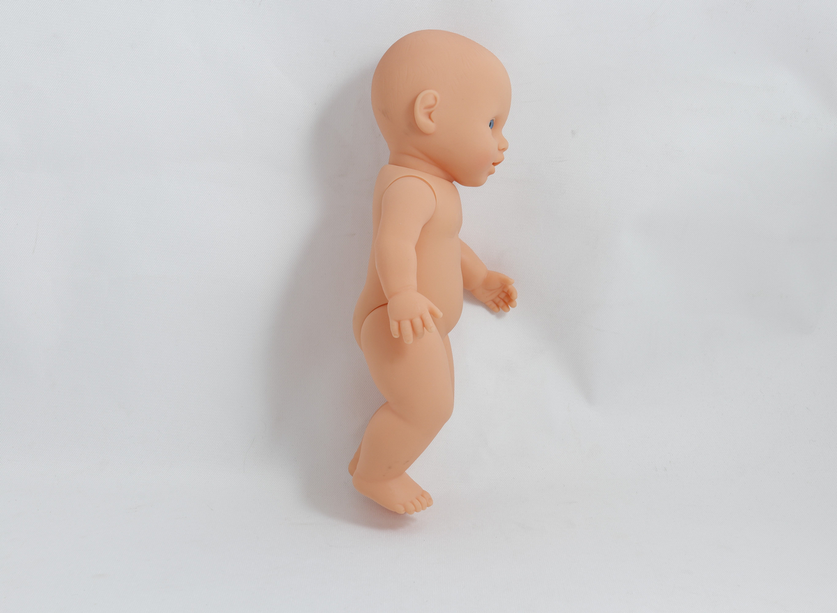 Babydukke, uten klær. Det er skrevet "Kristine" med tusj nederst på ryggen på dukka. 