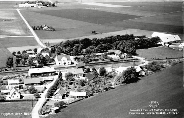 "Flygfoto över Brännarp" i Rävinge. Här startade 1938 Hallands Fruktindustri (HAFI) som fortfarande är verksamt. Där järnvägen korsar landsvägen ligger stationsbyggnaden, vilken fick detta utseende 1921 efter en kraftig ombyggnad. Stationen omges av ett fåtal villor och några lantgårdar med  ekonomibyggnader och omgivande odlingslandskap.