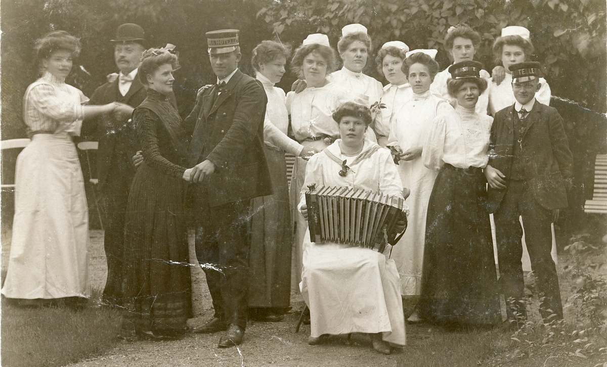 Foto av Olles syster Ida som spelar handklaver med människor i bakgrunden (enligt text skriven i albumet). Text på baksidan: "Hjärtliga hälsningar från syster Ida, skrif någon gång. Adresserat til servitören Herr Olof Svensson, Göteborg, Borensbergs Restaurang".