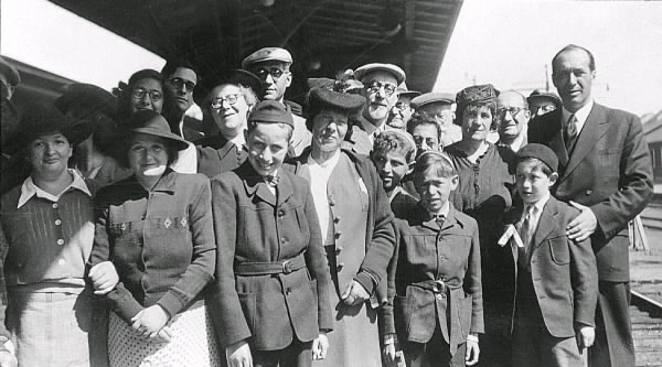 En grupp vuxna och barn fotograferade på järnvägsstationen i Varberg. Text med bilden: "En grupp av Helsjödanskarna". Uppgifter i övrigt saknas. Tillhör samlingen med fotokopior från Hallands Nyheter som är från 1930-1940-talen.