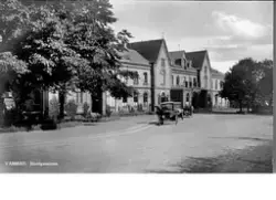 Vykort, "Varberg. Järnvägsstationen." Bilden tagen mot nordväst efter 1923 då den sydliga tillbyggnaden mot järnvägsparken gjordes (närmast i bild). Utmed Västra Vallgatan står några bilar parkerade.