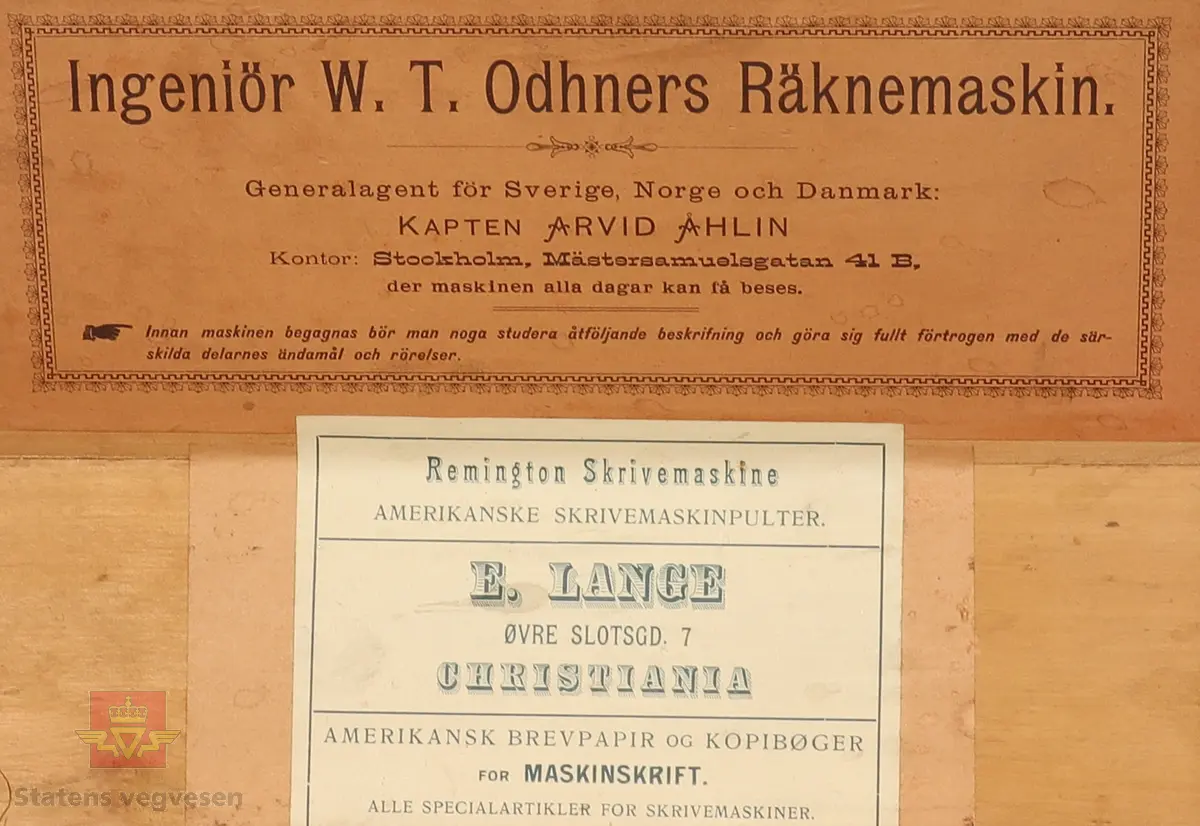 Mekanisk regnemaskin laget av metall som har et sveivehåndtak. Regnemaskinen sitter i en tre kasse med messinglås og trehåndtak. Regnemaskinen er gullfarget og svart, og er dekorert med logo. Sveivehåndtaker er sølv og brun farget og laget av tre. Inne i kisten henger en lapp. Det ligger også en liten nøkkel i kisten som hører til låsen. 