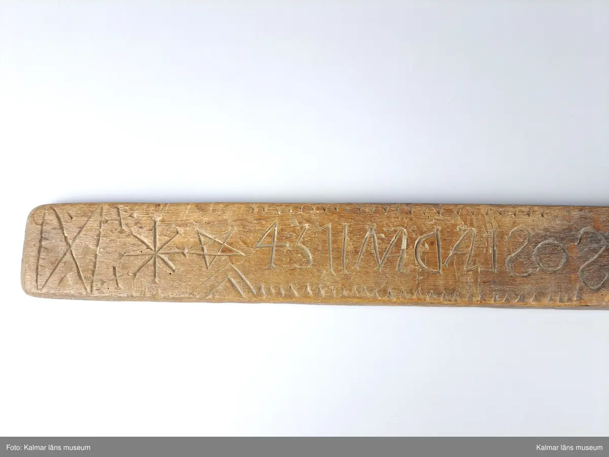 KLM 6438. Mangelbräde. Tillverkat av ek. Platt. Längs större delen av kanten vinkelband. Ytan har grovt inskurna tecken. Inskription bakvänd: SOS LAD AN 1734. Smalt men enkelt snidat handtag utan hästhuvud.