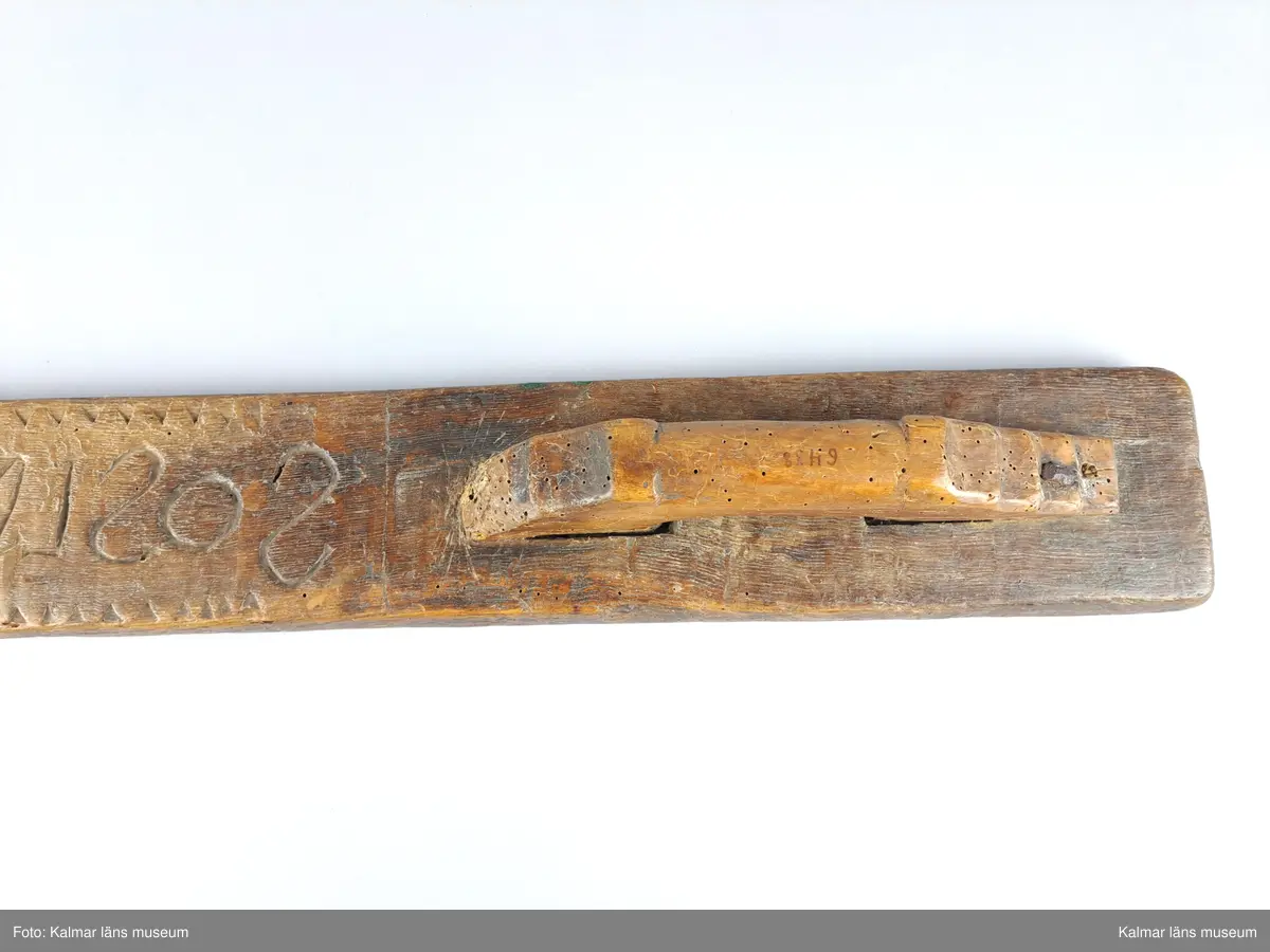 KLM 6438. Mangelbräde. Tillverkat av ek. Platt. Längs större delen av kanten vinkelband. Ytan har grovt inskurna tecken. Inskription bakvänd: SOS LAD AN 1734. Smalt men enkelt snidat handtag utan hästhuvud.