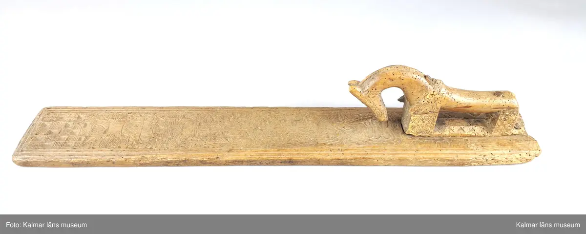 KLM 8325. Mangelbräde. Tillverkat av bok. Platt med kälade kanter. Ytan rikt ornerad med karvsnitt, cirklar, blommor, hjärtan m.m. Snidat handtag i form av en häst, något skadat. Inskrift: Anno 1786.