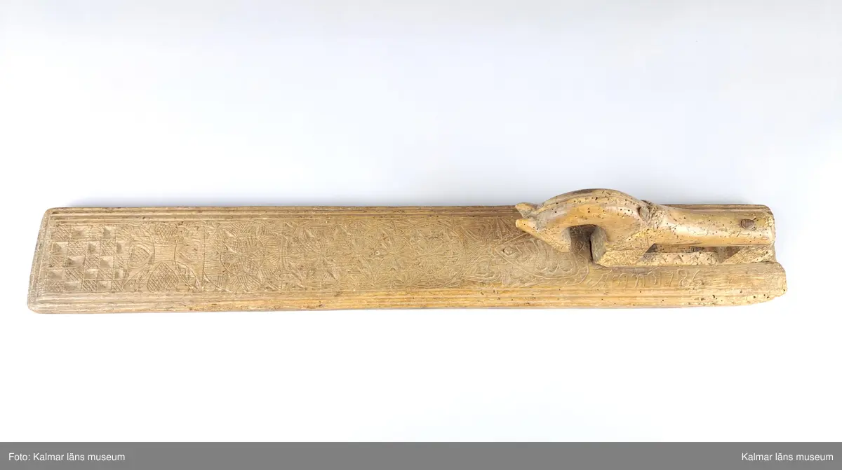 KLM 8325. Mangelbräde. Tillverkat av bok. Platt med kälade kanter. Ytan rikt ornerad med karvsnitt, cirklar, blommor, hjärtan m.m. Snidat handtag i form av en häst, något skadat. Inskrift: Anno 1786.