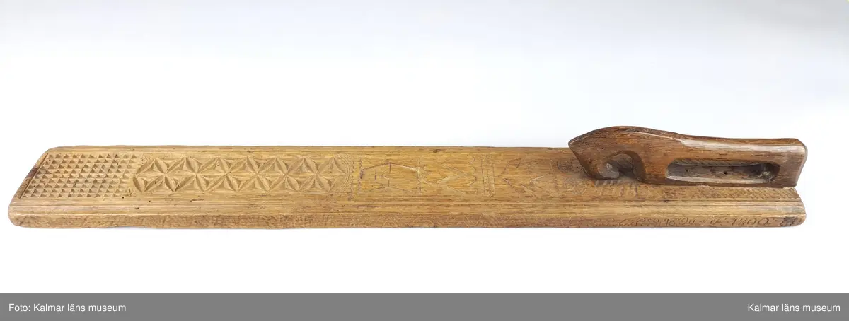 KLM 16532. Mangelbräde. Tillverkat av trä. Ytan med karvsnitt och plattskärningar, blommor, hjärtan, geometriska figurer. Snidat handtag i hästform. På ena sidan inskrift: S:P. C:P. d 16 juni 1800.