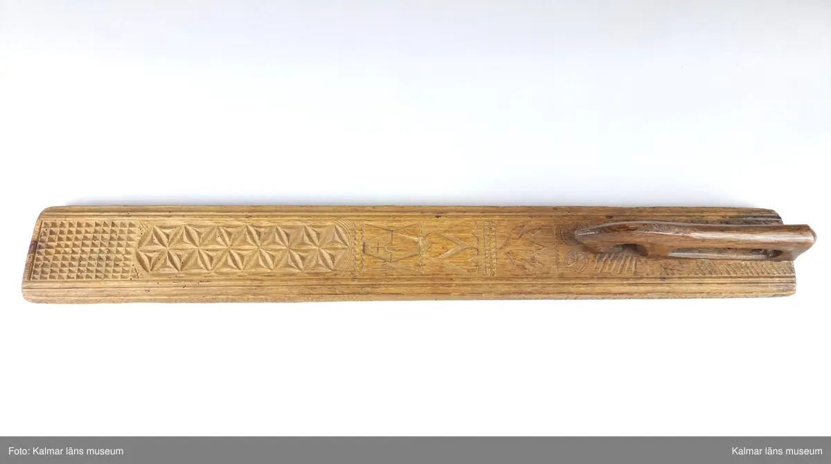 KLM 16532. Mangelbräde. Tillverkat av trä. Ytan med karvsnitt och plattskärningar, blommor, hjärtan, geometriska figurer. Snidat handtag i hästform. På ena sidan inskrift: S:P. C:P. d 16 juni 1800.