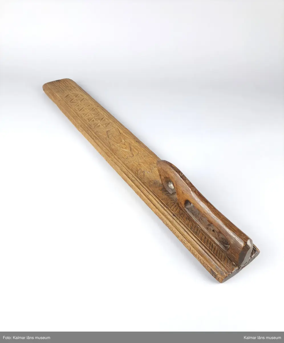 KLM 16532. Mangelbräde. Tillverkat av trä. Ytan med karvsnitt och plattskärningar, blommor, hjärtan, geometriska figurer. Snidat handtag i hästform. På ena sidan inskrift: S:P. C:P. d 16 juni 1800.