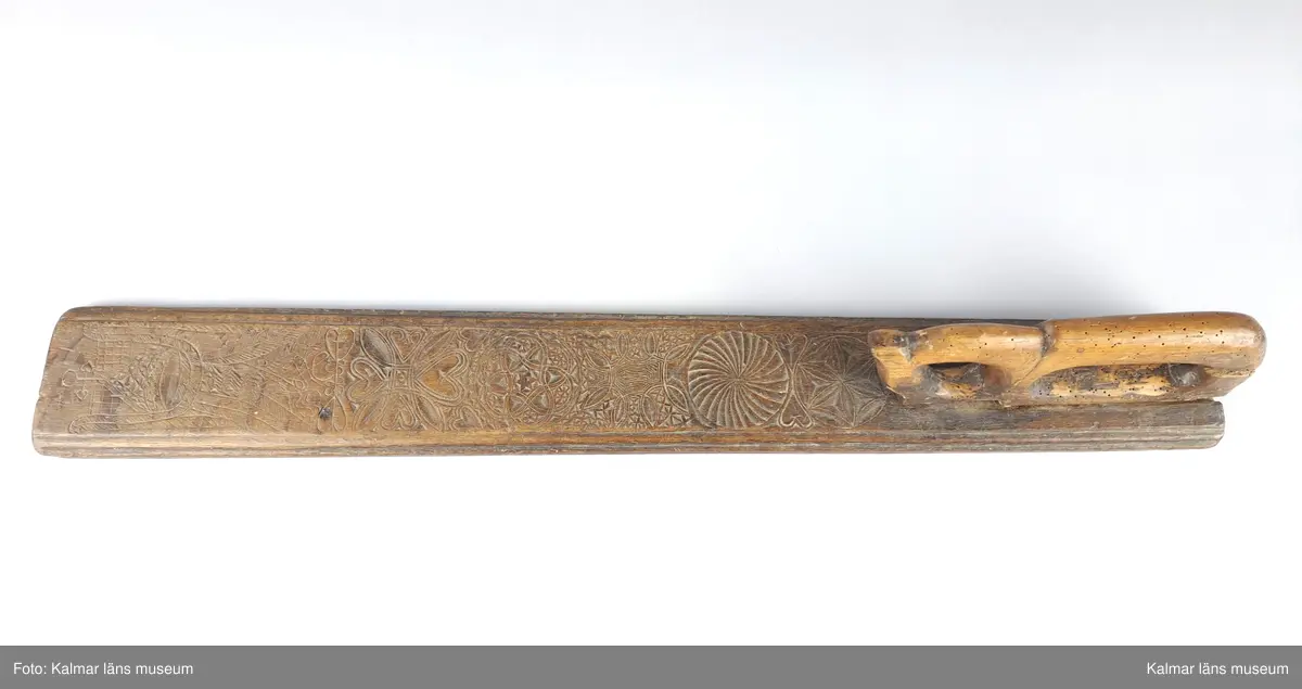 KLM 18017:1. Mangelbräde. Översida med rik karvsnittsornering. Snidat handtag i form av häst. På brädets bakre kortsida årtalet 1770.