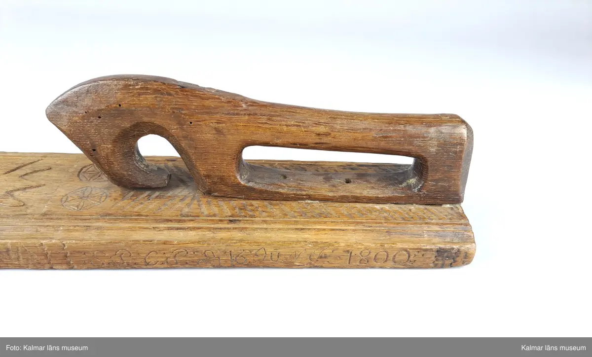 KLM 16532. Mangelbräde. Tillverkat av trä. Ytan med karvsnitt och plattskärningar, blommor, hjärtan, geometriska figurer. Snidat handtag i hästform. På ena sidan inskrift: S:P. C:P. d 16 juni 1800.