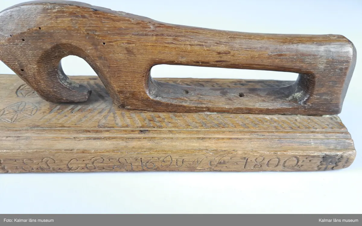 KLM 16532. Mangelbräde. Tillverkat av trä. Ytan med karvsnitt och plattskärningar, blommor, hjärtan, geometriska figurer. Snidat handtag i hästform. På ena sidan inskrift: S:P. C:P. d 16 juni 1800.