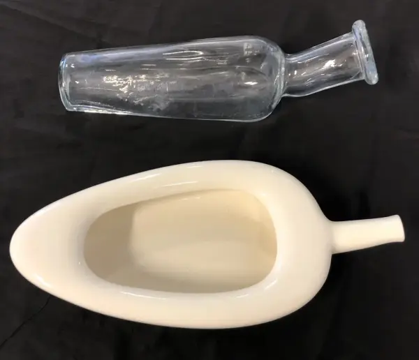 Bildet viser en avlang glassflaske og en kremhvit avlang gjenstand med åpning og tut