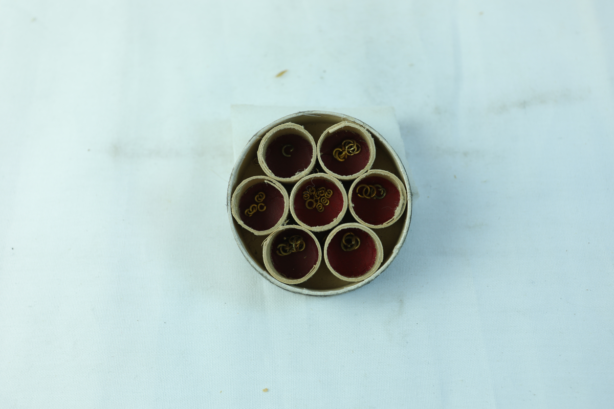 Liten rund pappboks til oppbevaring av ringer, trolig i gull.
