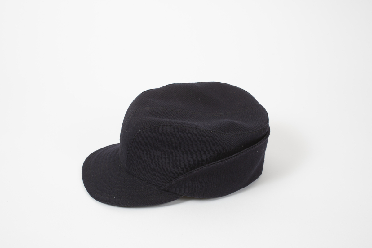 Lue/hatt tilhørende representasjonsdress fra vinterolympiaden i St Moritz 1948. Lua er av typen Holmenkolluen. Den er blå med solbrem foran,. Den har klaff som går fra foran ørene og helt rundt bak. Klaffen brettes opp utenpå lua.