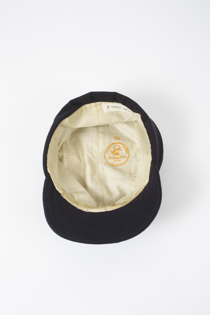 Lue/hatt tilhørende representasjonsdress fra vinterolympiaden i St Moritz 1948. Lua er av typen Holmenkolluen. Den er blå med solbrem foran,. Den har klaff som går fra foran ørene og helt rundt bak. Klaffen brettes opp utenpå lua.