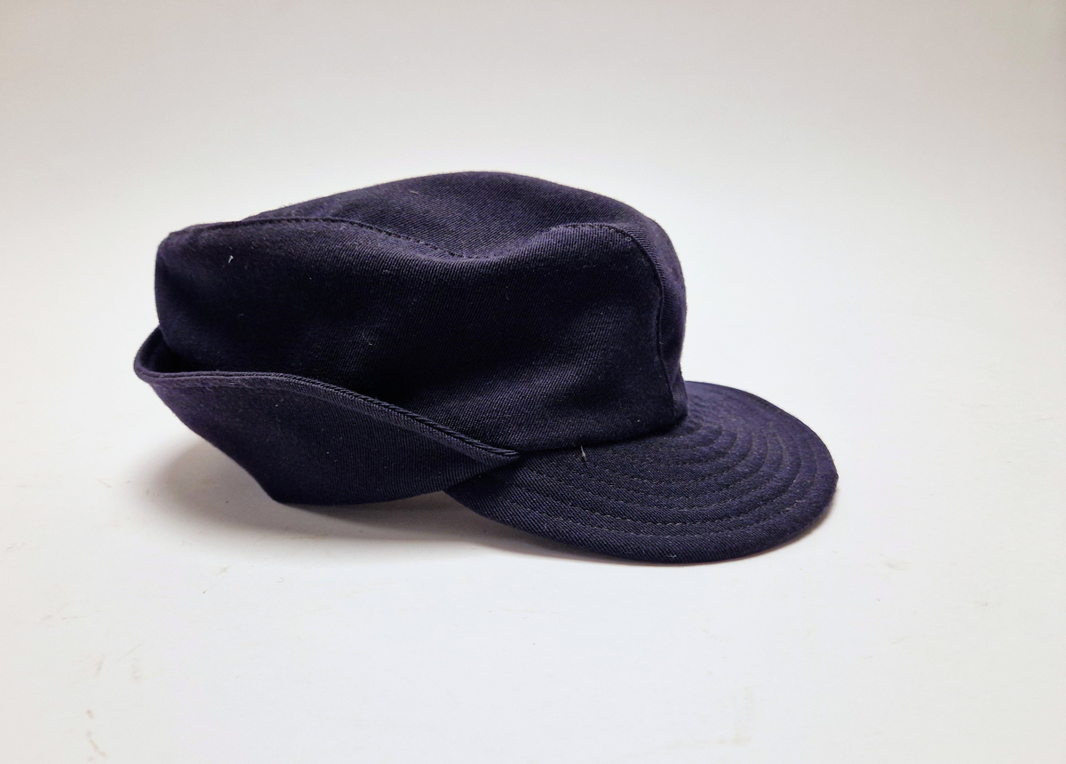 Lue/hatt tilhørende representasjonsdress fra vinterolympiaden i St Moritz 1948. Lua er av typen Holmenkolluen. Den er blå med solbrem foran,. Den har klaff som går fra foran ørene og helt rundt bak. Klaffen brettes opp utenpå lua.