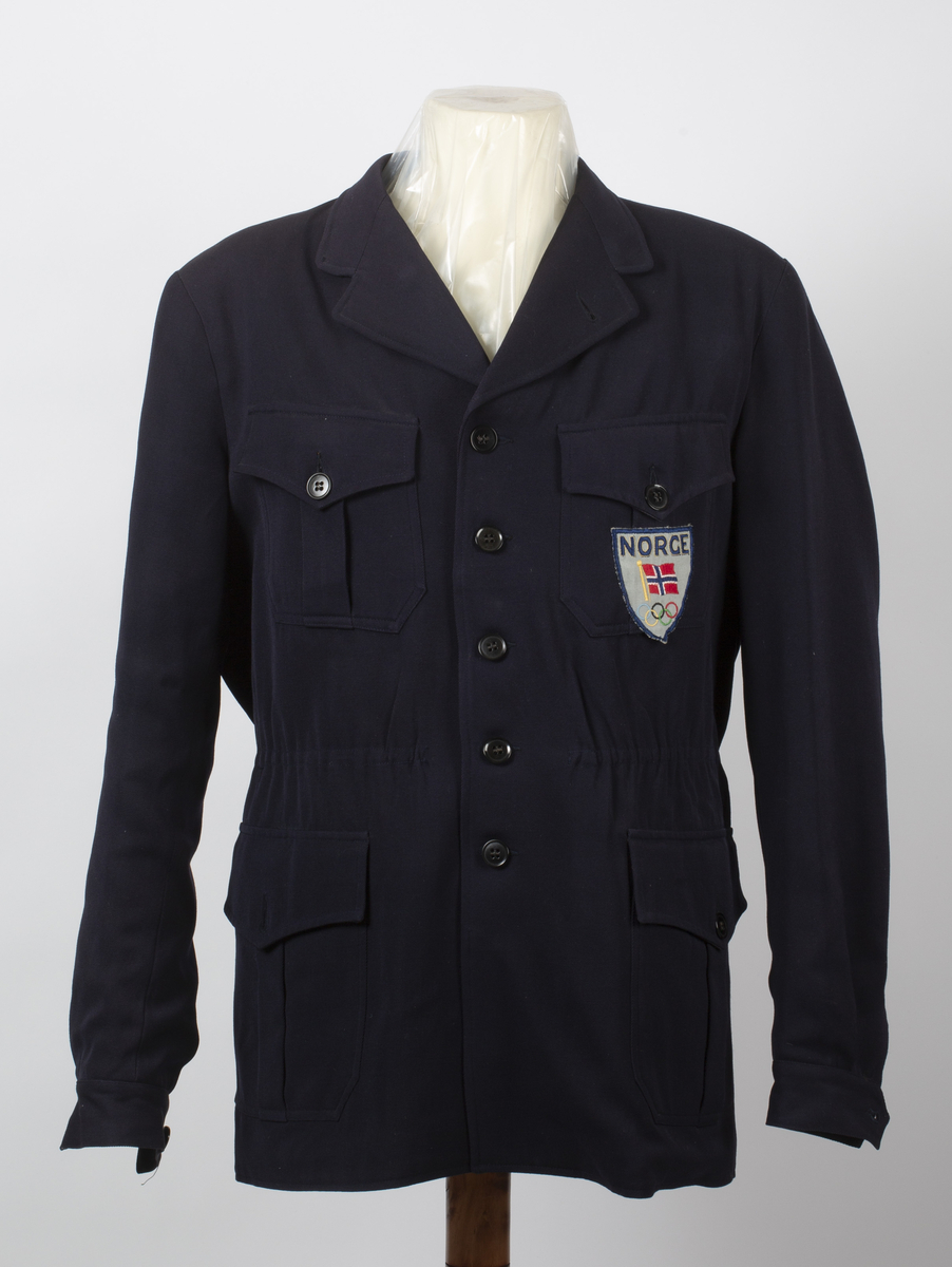 Representasjonsdressjakke fra vinterolympiaden i St Moritz 1948. Knepping foran med 5 knapper, 2 vanlige lommer og 2 brystlommer.
