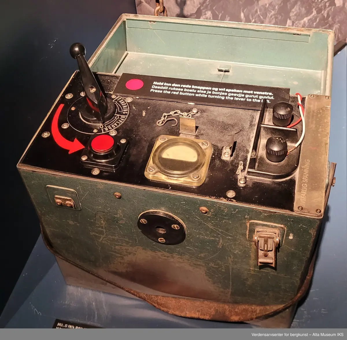Detonator i form av en metallboks med lokk. På innsiden finnes spake, brytere og måler.