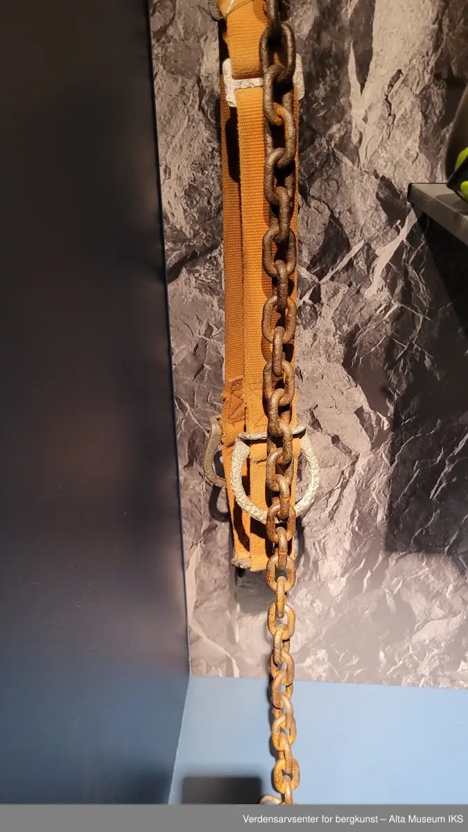Belte i oransje tekstil med tilkoblet metallkjetting.