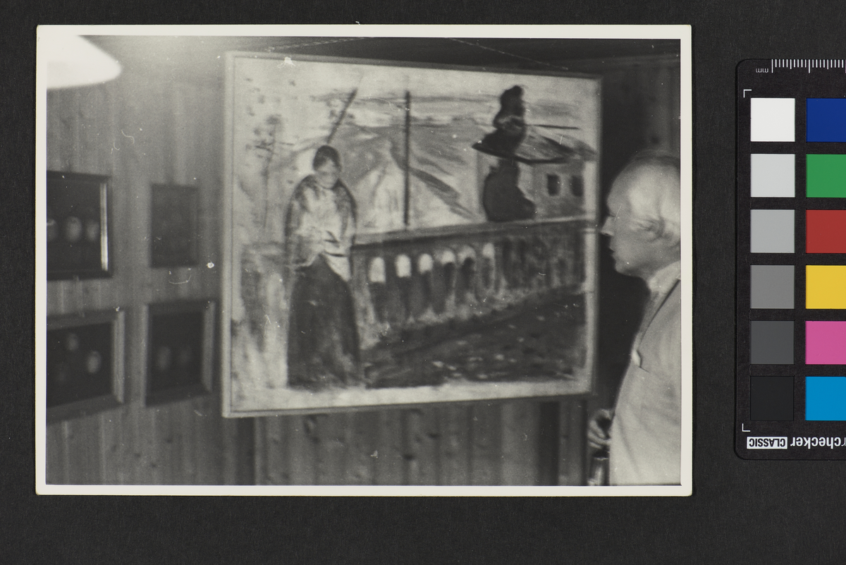 Til høyre i bildet står det en mann og ser på et stort maleri, som forestiller en kvinne ved rekkverket på en bro. I bakgrunnen er det bilder på en vegg dekket med trepanel.