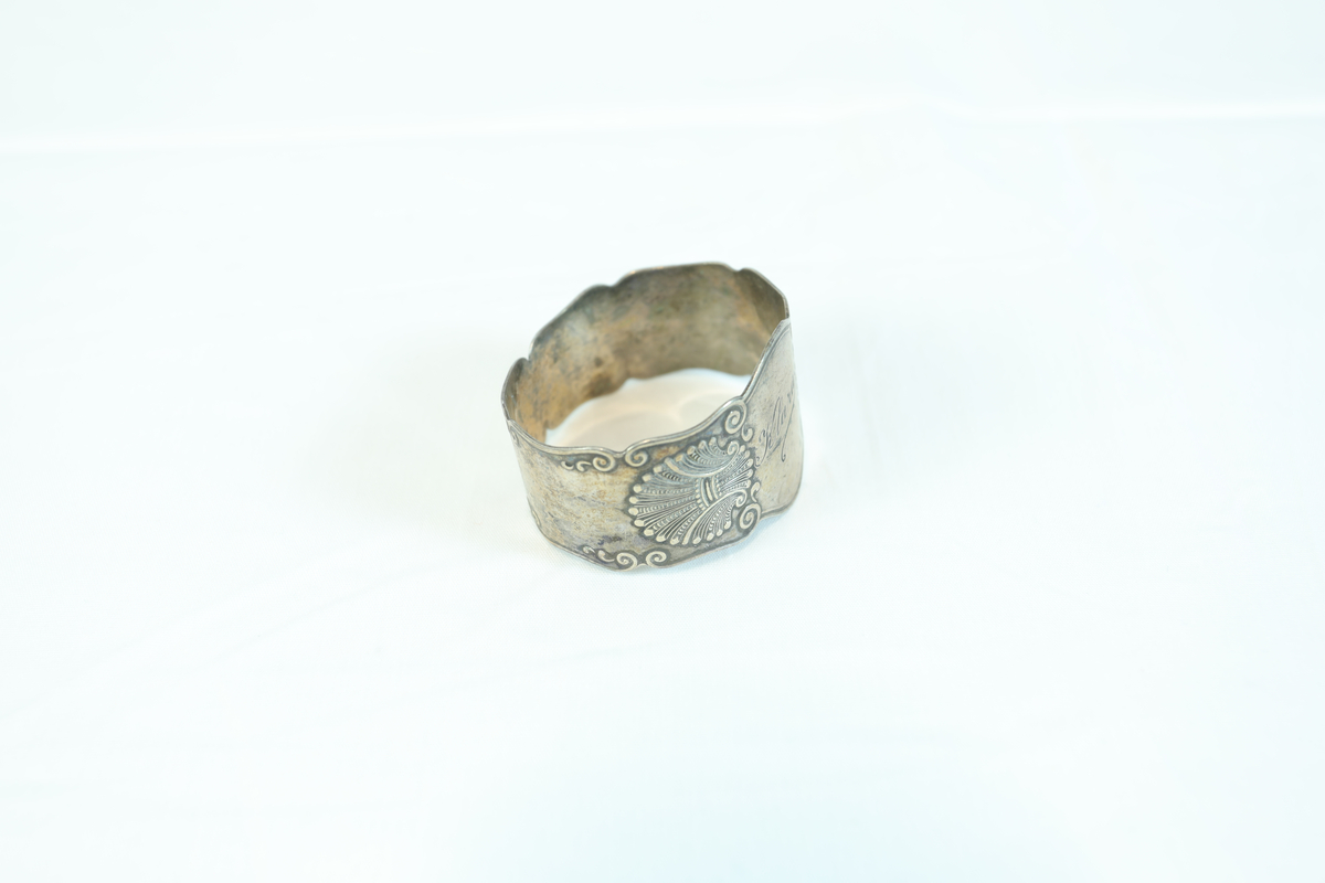 Lite og bredt armbånd i sølv eller tinn. Prydet med mønster og navnet "Klara" i løkkeskrift. 