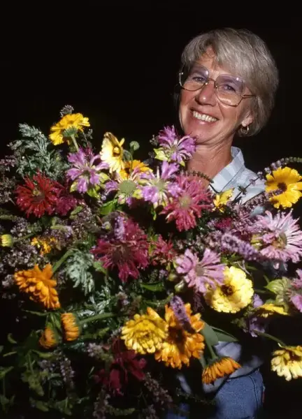 Cecilie Jensen, grunnlegger av Urtehagen på Domkirkeodden, står med favnen full av fargerike blomster.