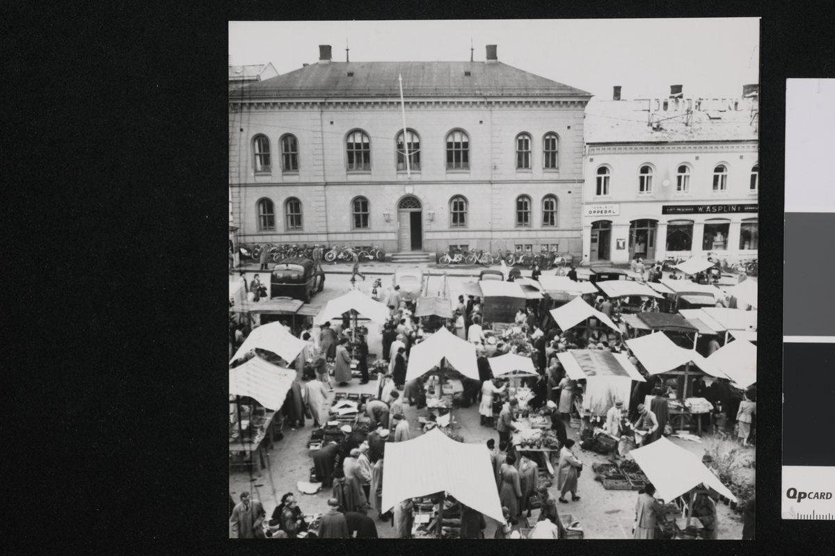 Tønsberg torg i fugleperspektiv, med folkevrimmel ved og rundt bodene. I bakgrunnen er det rader av bygninger og butikker.