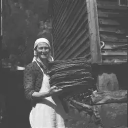 Kvinne i arbeidstøy med en stabel flatbrød. Bak henne sees h