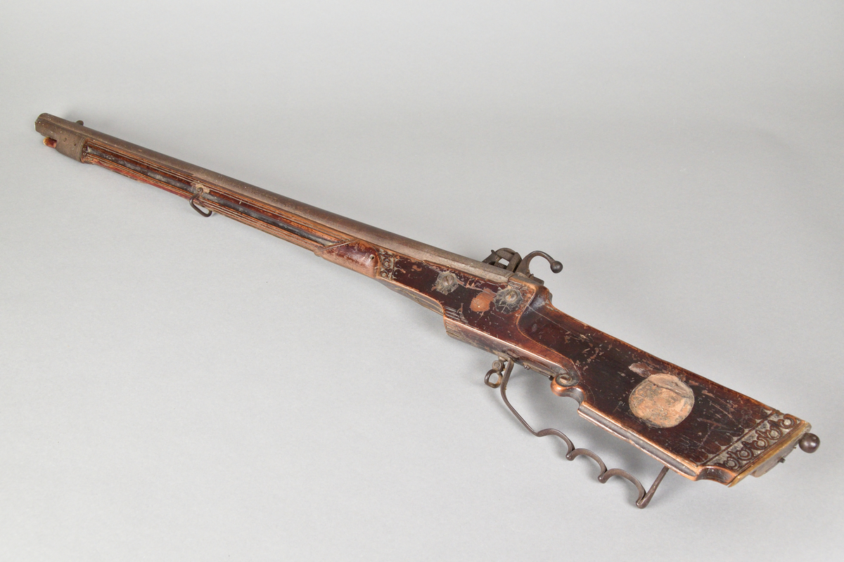 Hjullåsgevär tillverkad i metall och trä, troligtvis mahogny. Vanlig form med slätborrad pipa. Kolvens ände med skurna ornament samt en rund utskärning vilken troligtvis tidigare infattat ett ornament i annat material, men som nu saknas. Kolven även med låda med skjutlock. 
Ovansidan av geväret med inskuret årtal, "1651".Glas av mindre storlek för tex. starkvin eller likör. Glaskupa med graverat mönster. Slipad fyrkantig fot med inslipad stjärna i botten.