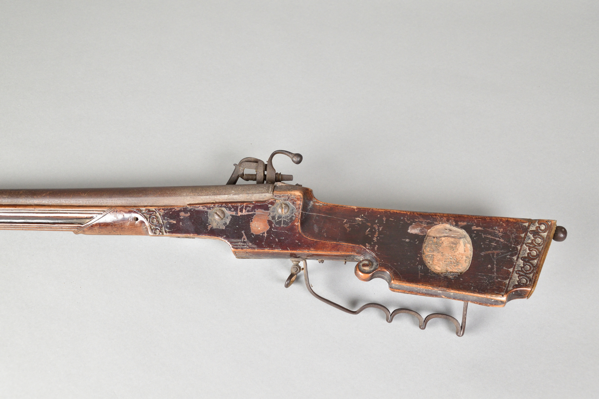 Hjullåsgevär tillverkad i metall och trä, troligtvis mahogny. Vanlig form med slätborrad pipa. Kolvens ände med skurna ornament samt en rund utskärning vilken troligtvis tidigare infattat ett ornament i annat material, men som nu saknas. Kolven även med låda med skjutlock. 
Ovansidan av geväret med inskuret årtal, "1651".Glas av mindre storlek för tex. starkvin eller likör. Glaskupa med graverat mönster. Slipad fyrkantig fot med inslipad stjärna i botten.