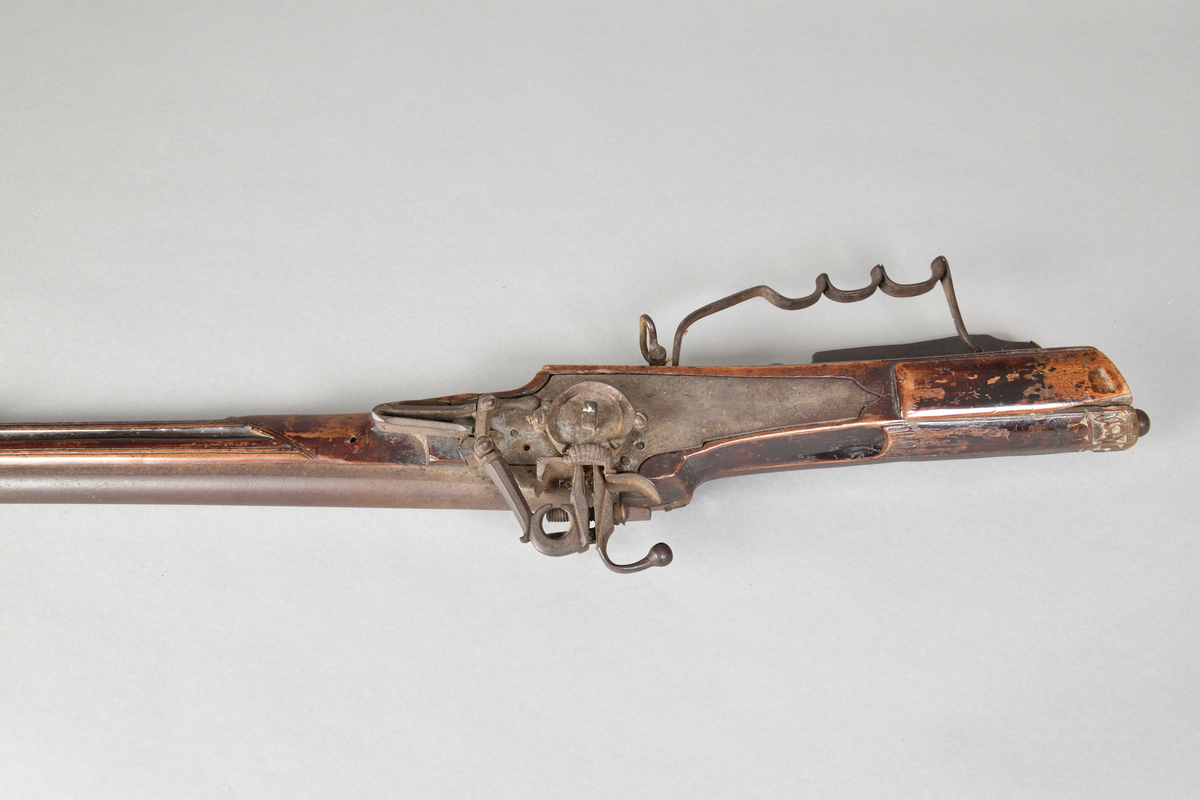 Hjullåsgevär tillverkad i metall och trä, troligtvis mahogny. Vanlig form med slätborrad pipa. Kolvens ände med skurna ornament samt en rund utskärning vilken troligtvis tidigare infattat ett ornament i annat material, men som nu saknas. Kolven även med låda med skjutlock. 
Ovansidan av geväret med inskuret årtal, "1651".Glas av mindre storlek för tex. starkvin eller likör. Glaskupa med graverat mönster. Slipad fyrkantig fot med inslipad stjärna i botten.