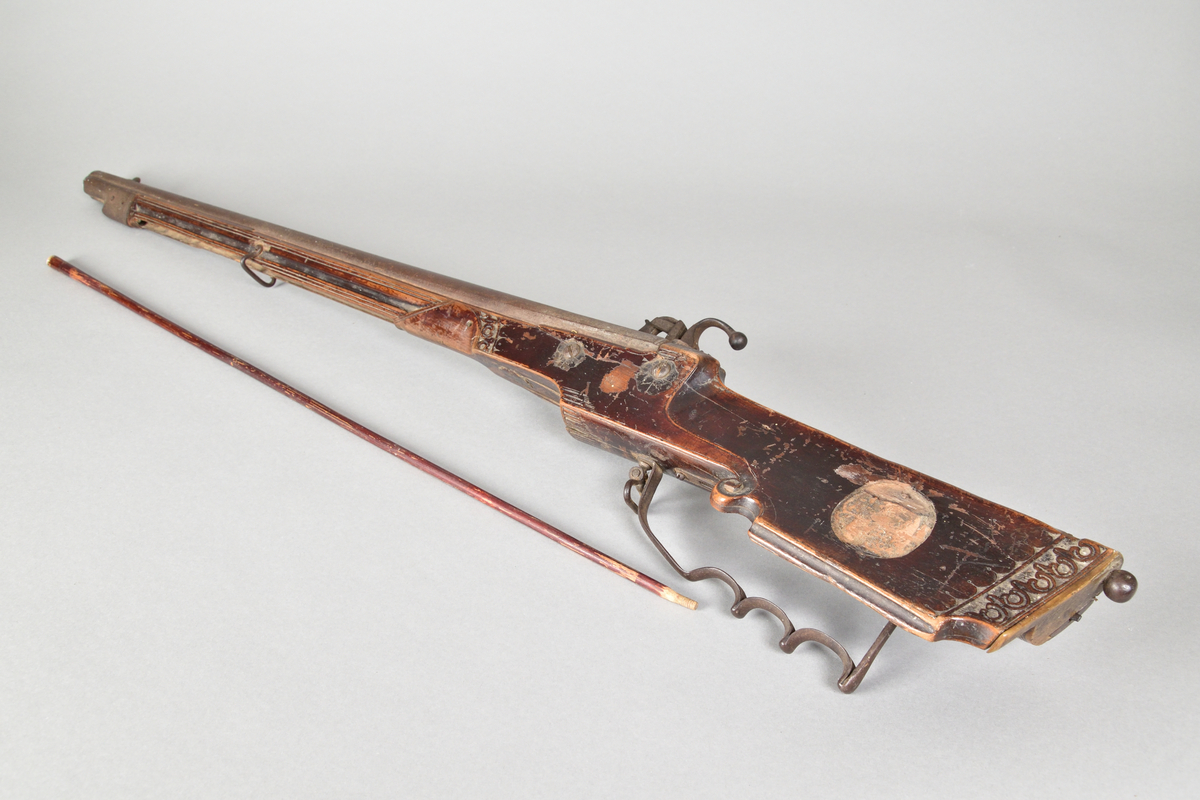 Hjullåsgevär tillverkad i metall och trä, troligtvis mahogny. Vanlig form med slätborrad pipa. Kolvens ände med skurna ornament samt en rund utskärning vilken troligtvis tidigare infattat ett ornament i annat material, men som nu saknas. Kolven även med låda med skjutlock. 
Ovansidan av geväret med inskuret årtal, "1651".Glas av mindre storlek för tex. starkvin eller likör. Glaskupa med graverat mönster. Slipad fyrkantig fot med inslipad stjärna i botten.