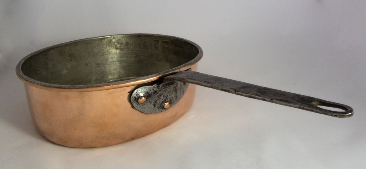 Kastrull med lock tillverkad i koppar. Oval form med raka sidor. Lockets handtag har hjärtbladsformade fästen. Kastrullen har ett handtag av järn med ett halvcirkelformat fäste.