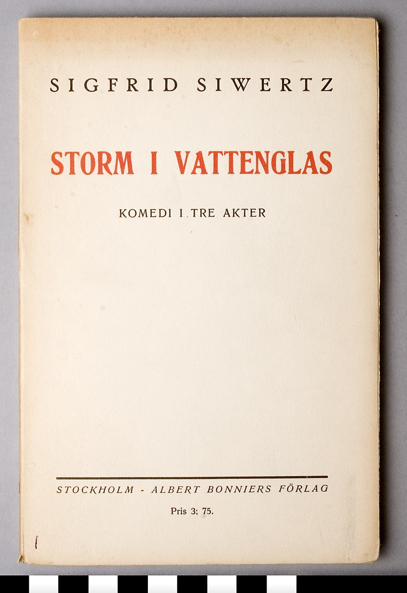Bok, i pappersband. Fram- och baksida av tunn kartong, beige, med tryck i svart och rött: SIGFRID SIWERTZ STORM I VATTENGLAS KOMEDI I TRE AKTER,  tryckeri och ort samt priset, 3:75. 116 sidor ej uppskurna.