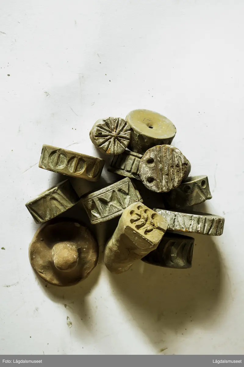Samling av 11 ulike trykkblokker/stempel i keramikk, et målebånd og keramikkbollen de ble oppbevart i i Hansens verksted.