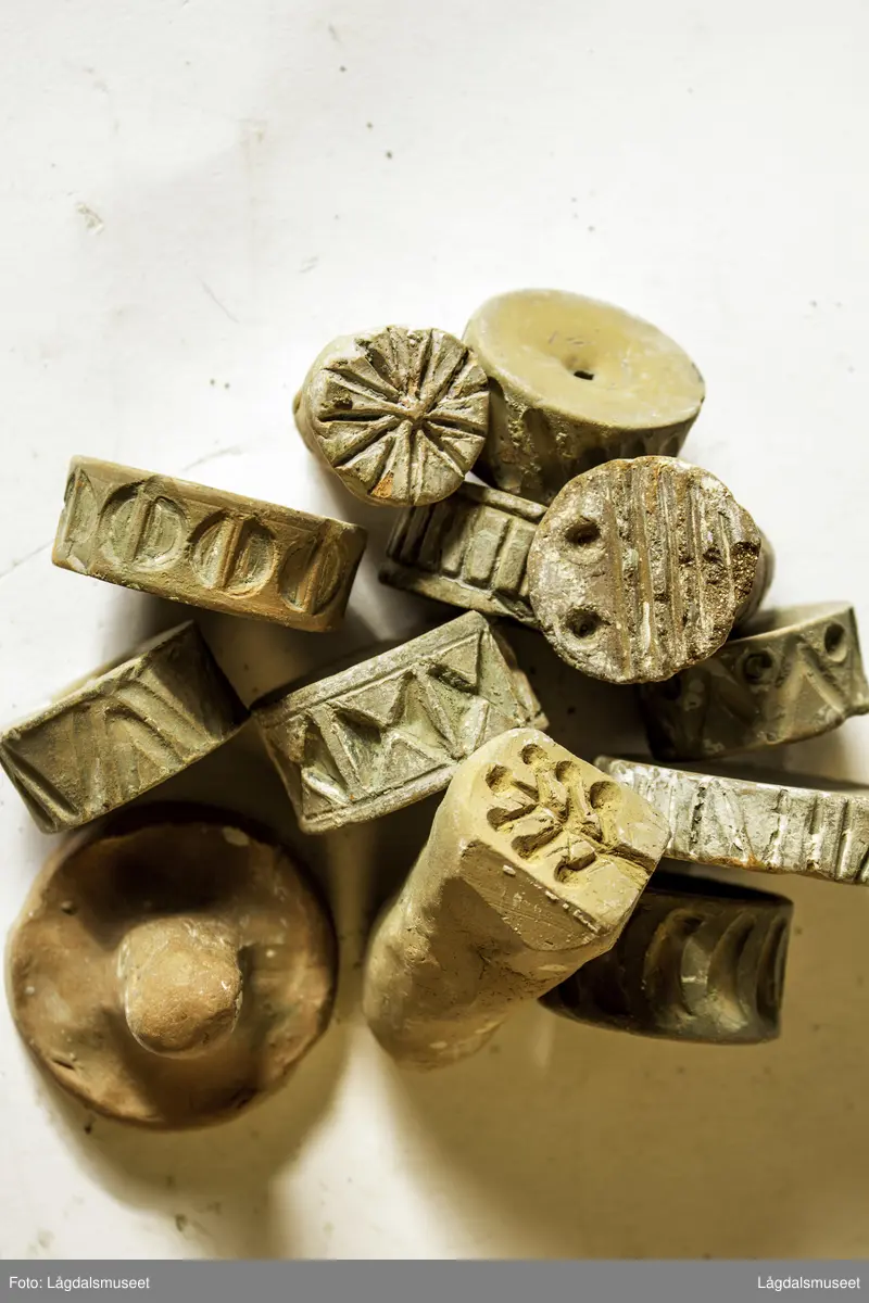 Samling av 11 ulike trykkblokker/stempel i keramikk, et målebånd og keramikkbollen de ble oppbevart i i Hansens verksted.